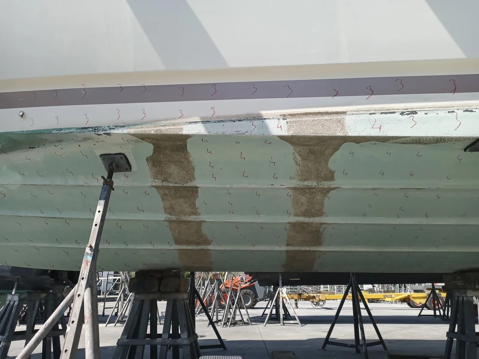 Karaya alınmış motoryatın karinası: takozlar üzerinde, antifouling ve su hattı görünüyor